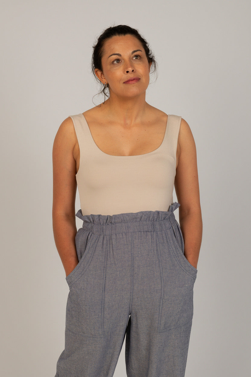 Woman wearing a beige tank top and gray pants on a white background