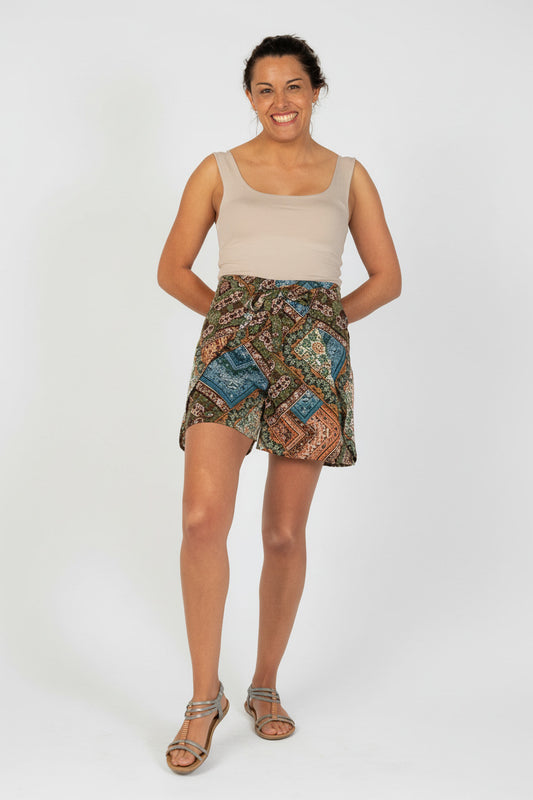 Woman wearing patterned shorts and beige top on a white background